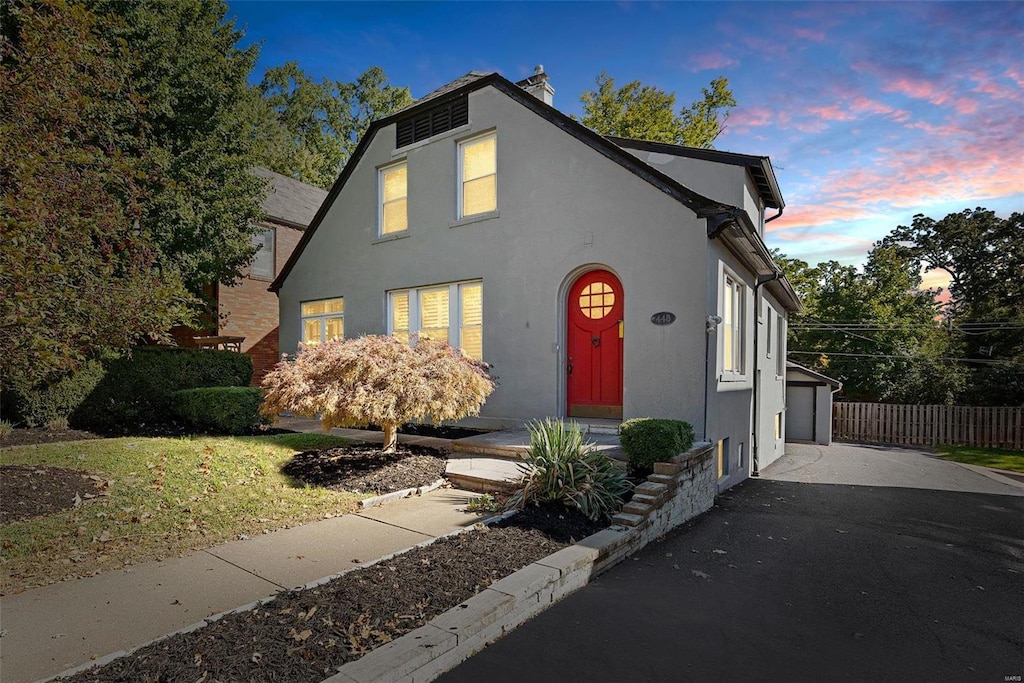 view of front of property featuring driveway, a chimney, fence, and stucco siding