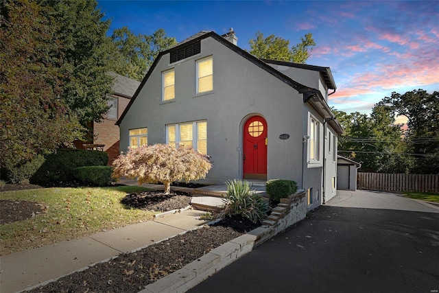 view of front of property featuring driveway, a chimney, fence, and stucco siding