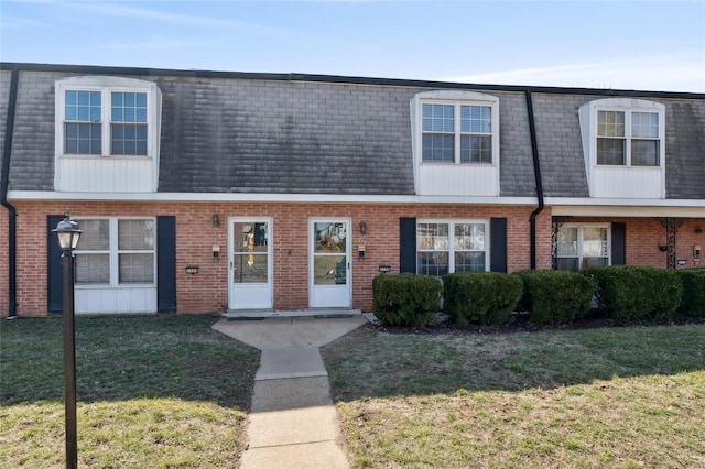 view of property with a shingled roof, a front lawn, mansard roof, and brick siding