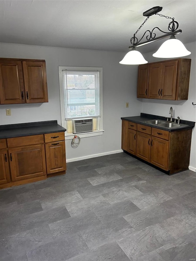 kitchen featuring brown cabinets, decorative light fixtures, dark countertops, a sink, and baseboards