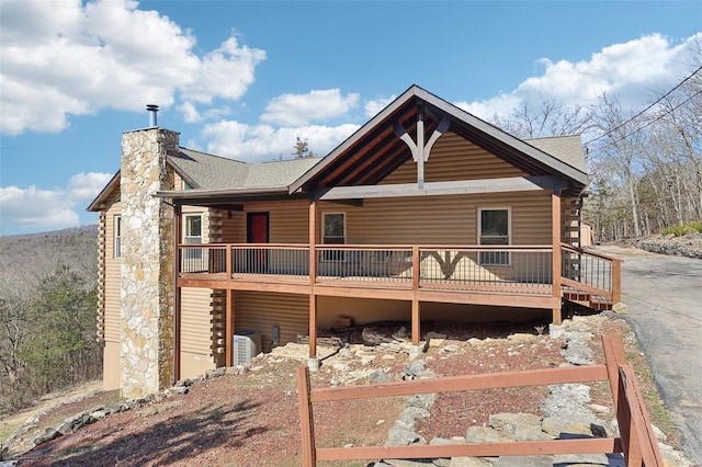 view of front facade with central AC unit, roof with shingles, log siding, a chimney, and a deck