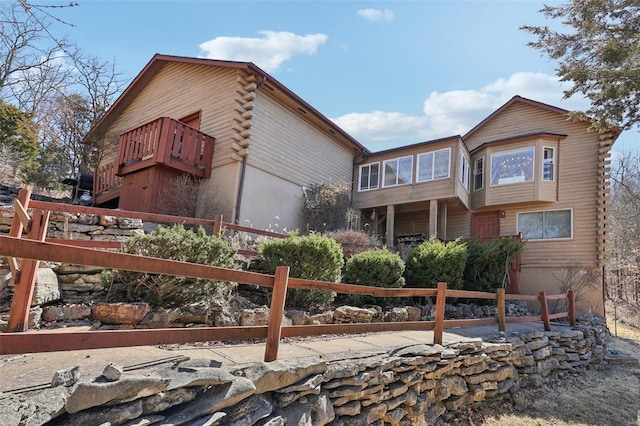 view of property exterior with a balcony, log exterior, and fence