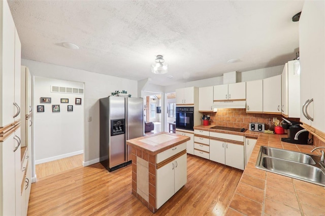 kitchen with a center island, tile counters, under cabinet range hood, black appliances, and a sink