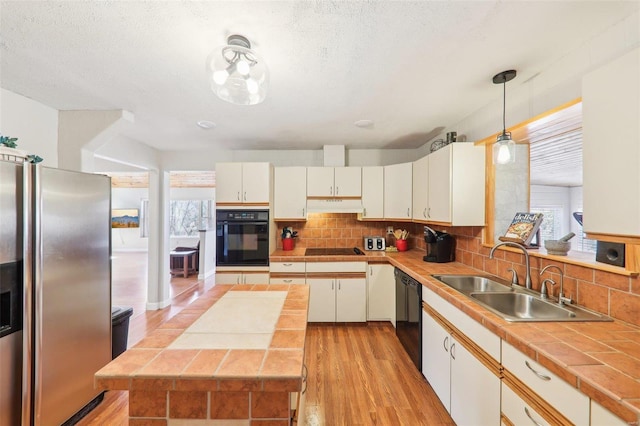 kitchen featuring black appliances, a sink, under cabinet range hood, backsplash, and light wood-style floors