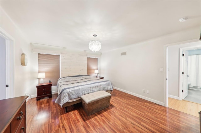 bedroom with a notable chandelier, wood finished floors, visible vents, and baseboards