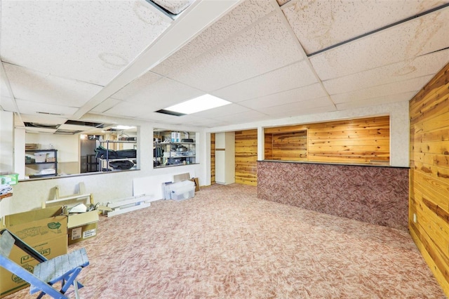 finished basement featuring a drop ceiling, wood walls, and carpet