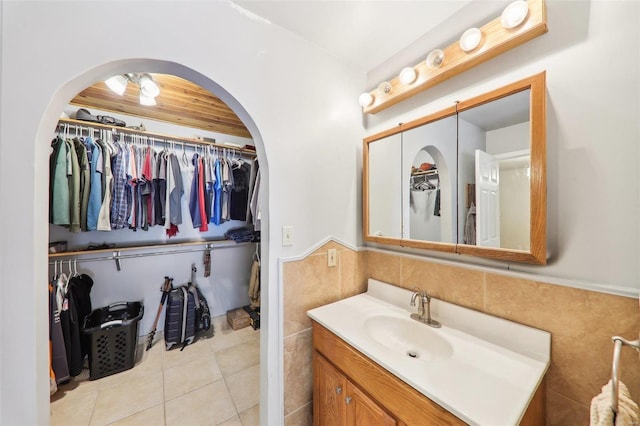 bathroom with tile patterned flooring, a walk in closet, a wainscoted wall, vanity, and tile walls