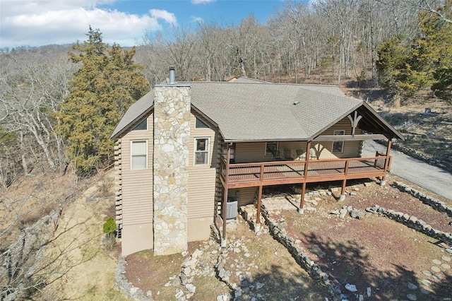 exterior space with a wooden deck, central air condition unit, a forest view, and a chimney