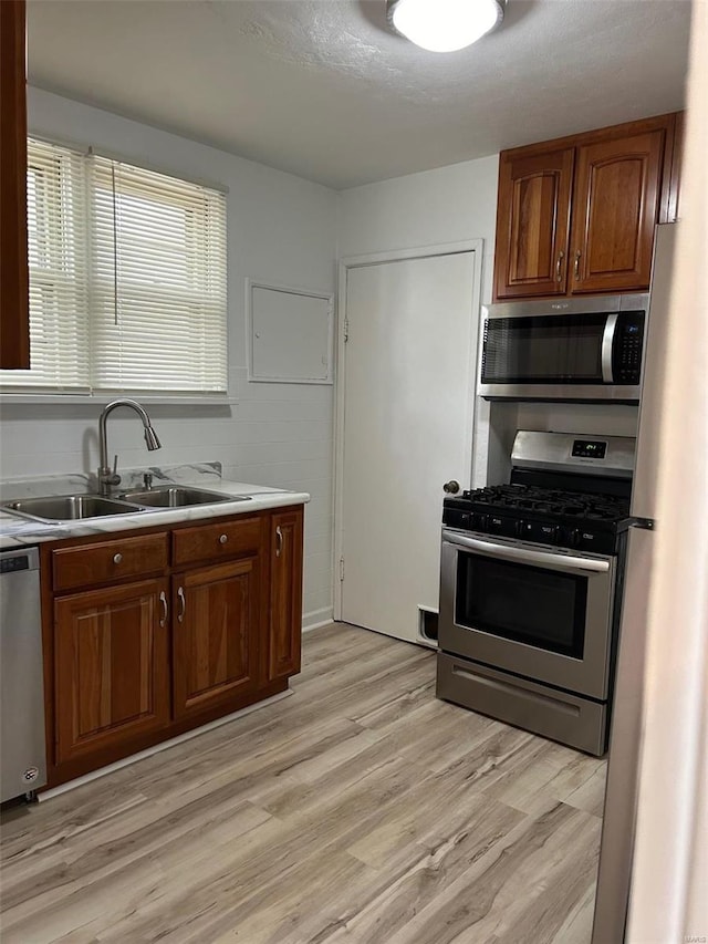 kitchen featuring light wood finished floors, brown cabinetry, appliances with stainless steel finishes, light countertops, and a sink