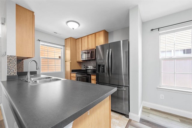 kitchen featuring a wealth of natural light, a sink, backsplash, stainless steel appliances, and a peninsula