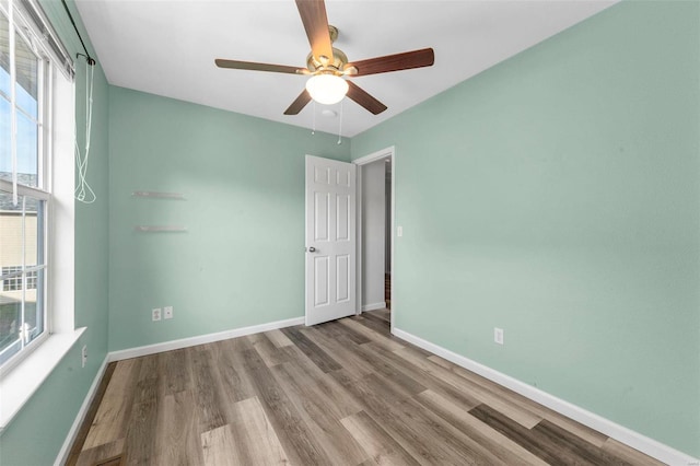 spare room featuring baseboards, wood finished floors, and a ceiling fan