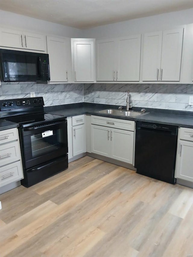 kitchen featuring dark countertops, black appliances, light wood-type flooring, and a sink