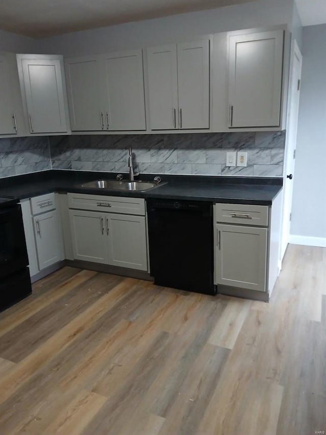 kitchen with black dishwasher, dark countertops, light wood-style flooring, a sink, and backsplash