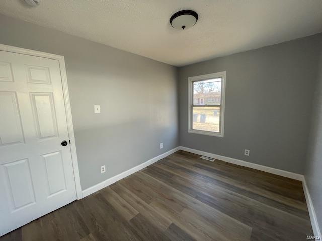 spare room featuring dark wood-style floors, visible vents, and baseboards