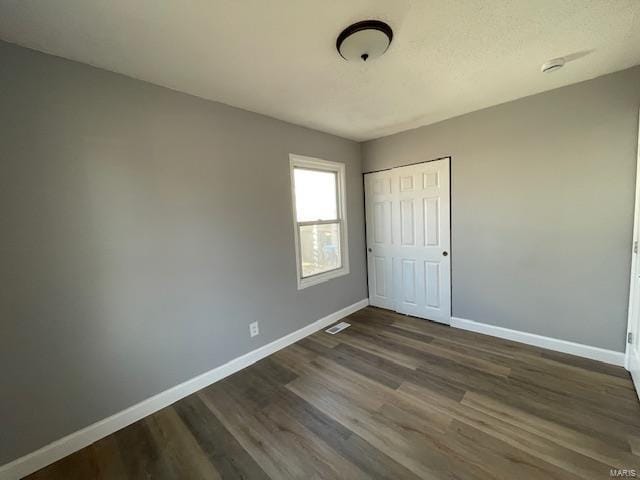 unfurnished bedroom with visible vents, baseboards, dark wood finished floors, and a closet