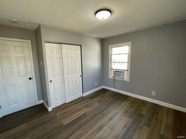 unfurnished bedroom featuring baseboards, dark wood finished floors, cooling unit, a textured ceiling, and a closet