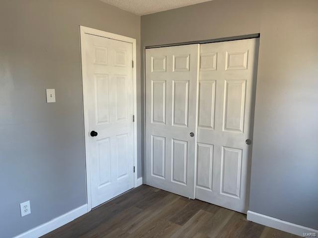 unfurnished bedroom with a textured ceiling, dark wood-type flooring, a closet, and baseboards
