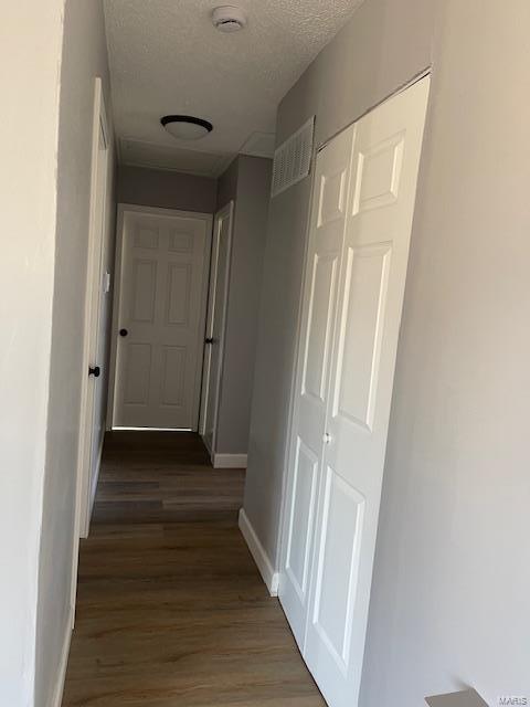 corridor with baseboards, visible vents, a textured ceiling, and wood finished floors