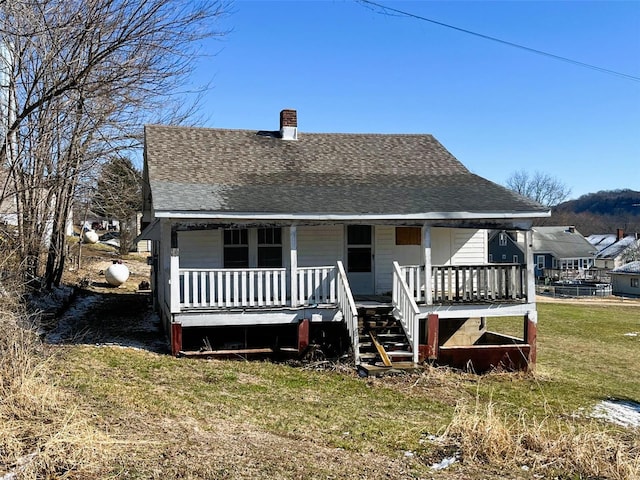 rear view of property featuring roof with shingles, a porch, and a lawn