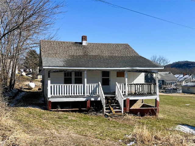 rear view of house featuring a porch, a yard, and a shingled roof