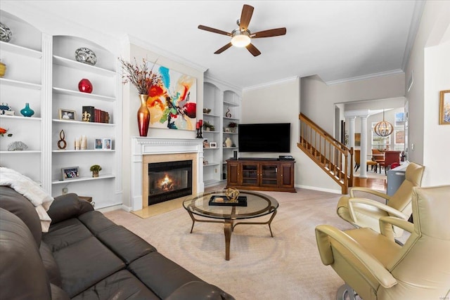 carpeted living room featuring built in shelves, baseboards, ornamental molding, a glass covered fireplace, and decorative columns