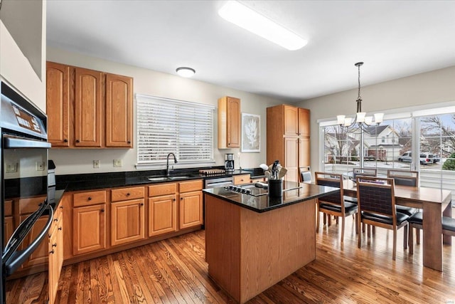 kitchen featuring wood finished floors, a center island, a chandelier, pendant lighting, and a sink