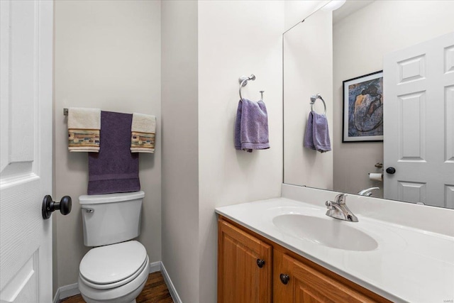 half bath with baseboards, vanity, and toilet