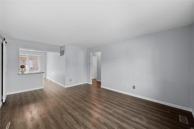 unfurnished living room featuring a barn door, visible vents, dark wood-type flooring, and baseboards