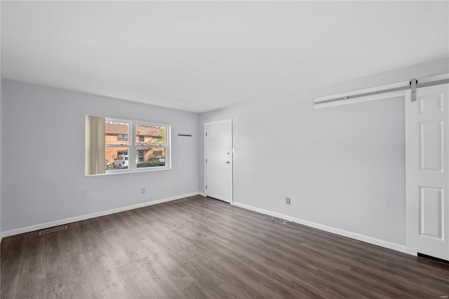 empty room featuring a barn door, baseboards, visible vents, and dark wood-style flooring