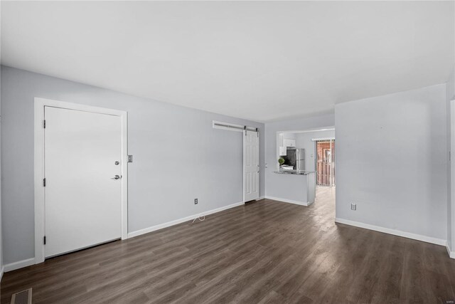 unfurnished living room featuring dark wood-style floors, visible vents, baseboards, and a barn door