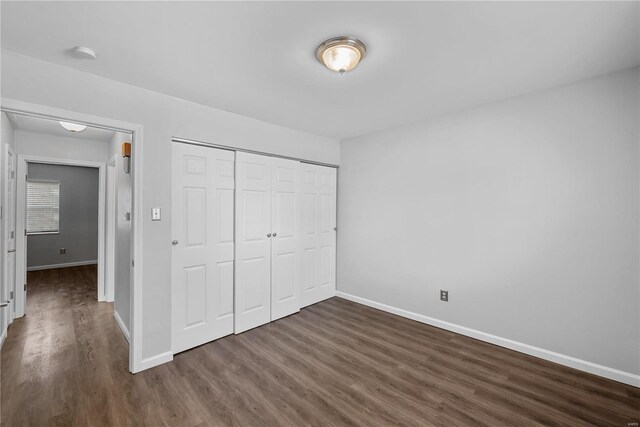 unfurnished bedroom featuring baseboards, dark wood-style flooring, and a closet