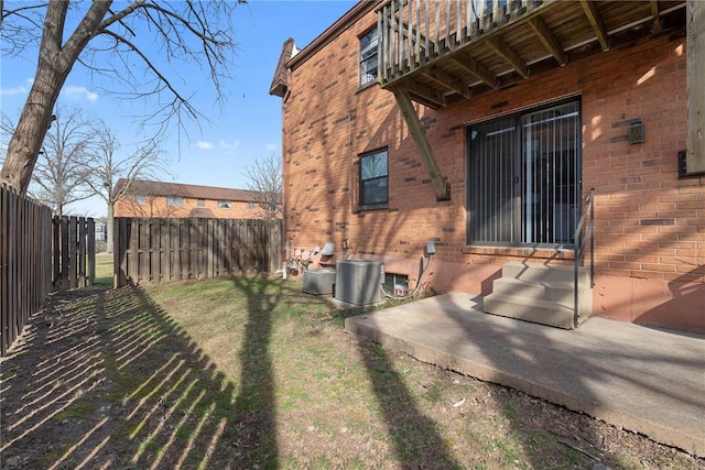 exterior space with central air condition unit, brick siding, a fenced backyard, and a lawn