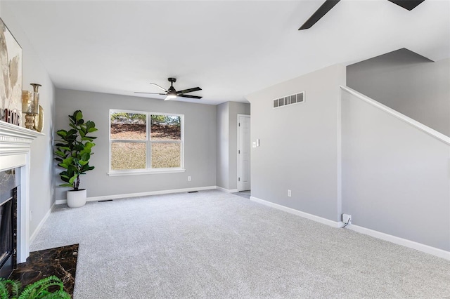 unfurnished living room with a high end fireplace, visible vents, baseboards, carpet floors, and a ceiling fan