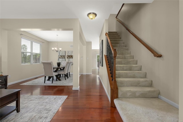 foyer entrance with visible vents, wood finished floors, stairway, baseboards, and an inviting chandelier