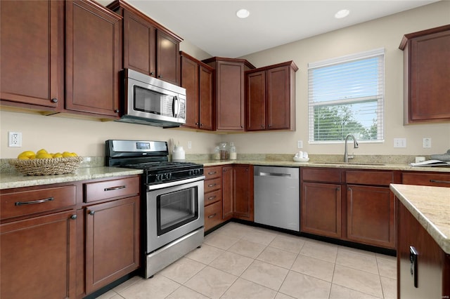 kitchen featuring recessed lighting, light stone counters, a sink, light tile patterned floors, and stainless steel appliances
