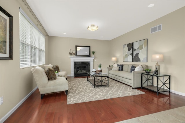 living area with a fireplace with flush hearth, baseboards, wood finished floors, and visible vents
