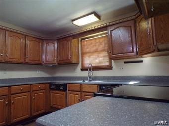 kitchen featuring dark countertops, brown cabinets, dishwasher, and a sink