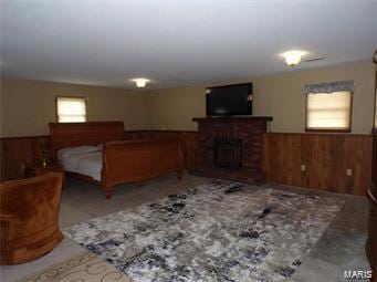 bedroom with a brick fireplace, a wainscoted wall, wood walls, and multiple windows