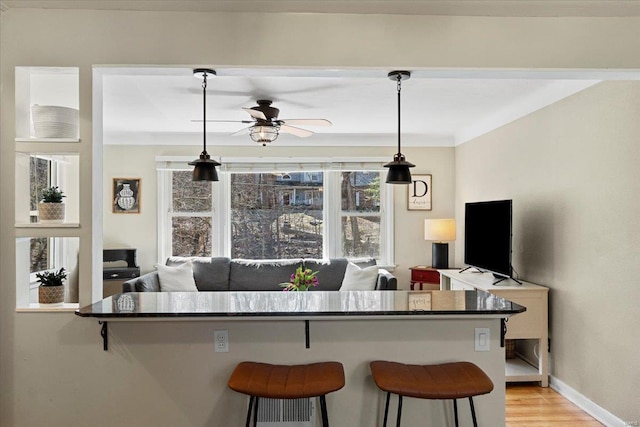 kitchen with ceiling fan, light wood-type flooring, decorative light fixtures, and a kitchen breakfast bar