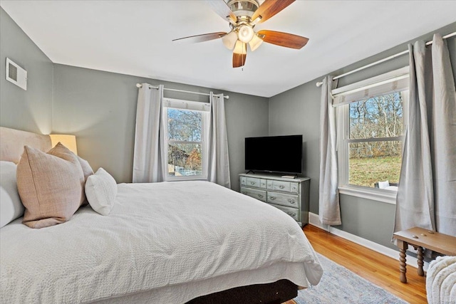 bedroom featuring a ceiling fan, visible vents, baseboards, and wood finished floors