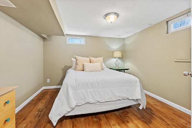 bedroom with visible vents, a textured ceiling, baseboards, and wood finished floors