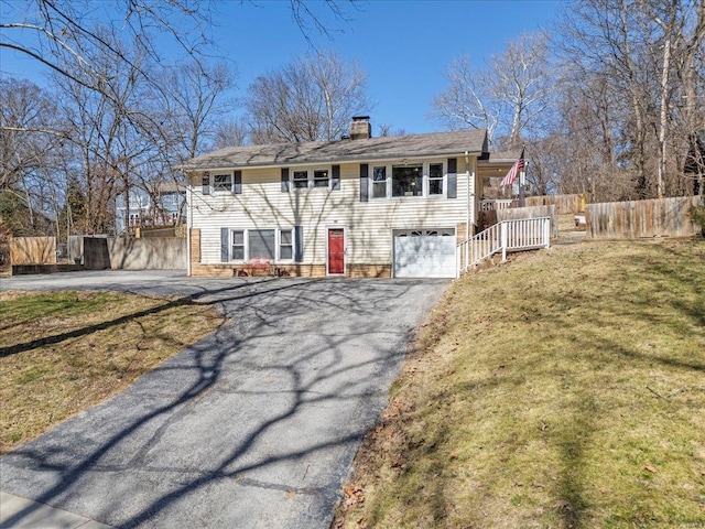 view of front facade with a chimney, fence, a garage, driveway, and a front lawn