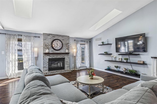 living room featuring wood finished floors, visible vents, baseboards, vaulted ceiling with skylight, and a brick fireplace