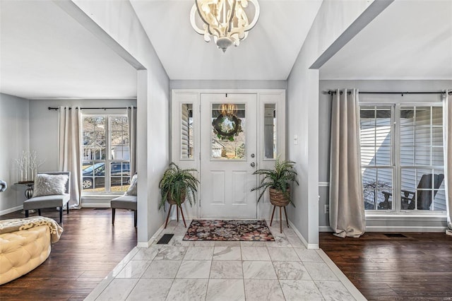 foyer featuring a chandelier, baseboards, lofted ceiling, and wood finished floors