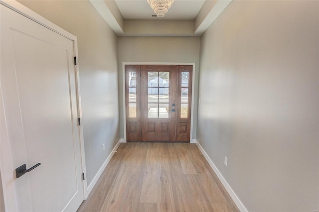 doorway with baseboards, a tray ceiling, and light wood-style floors