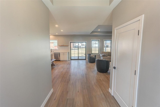 hallway featuring a tray ceiling, recessed lighting, wood finished floors, and baseboards