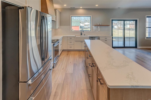 kitchen with a sink, light wood-style floors, light countertops, appliances with stainless steel finishes, and decorative backsplash