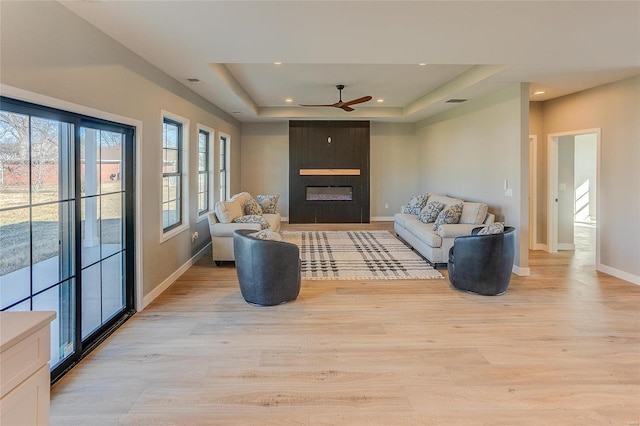 living room with a raised ceiling, a large fireplace, and light wood finished floors