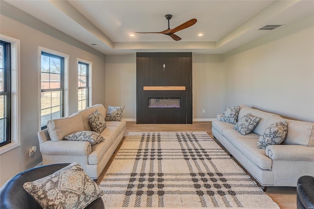 living room with visible vents, a fireplace, a tray ceiling, and wood finished floors