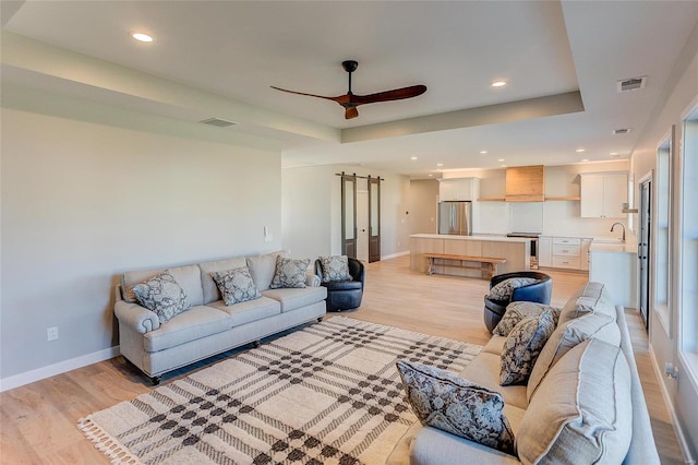 living room with baseboards, visible vents, ceiling fan, a tray ceiling, and light wood-style floors